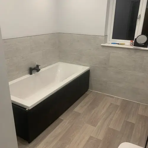 Renovated bathroom with a black bath panel and wood-effect floor