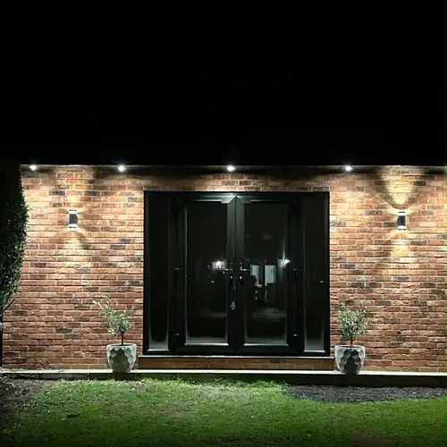 Brick-clad garden room with French doors and wall lights at night