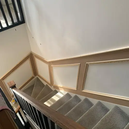 Panelled staircase wall with an oak handrail and grey stair carpet