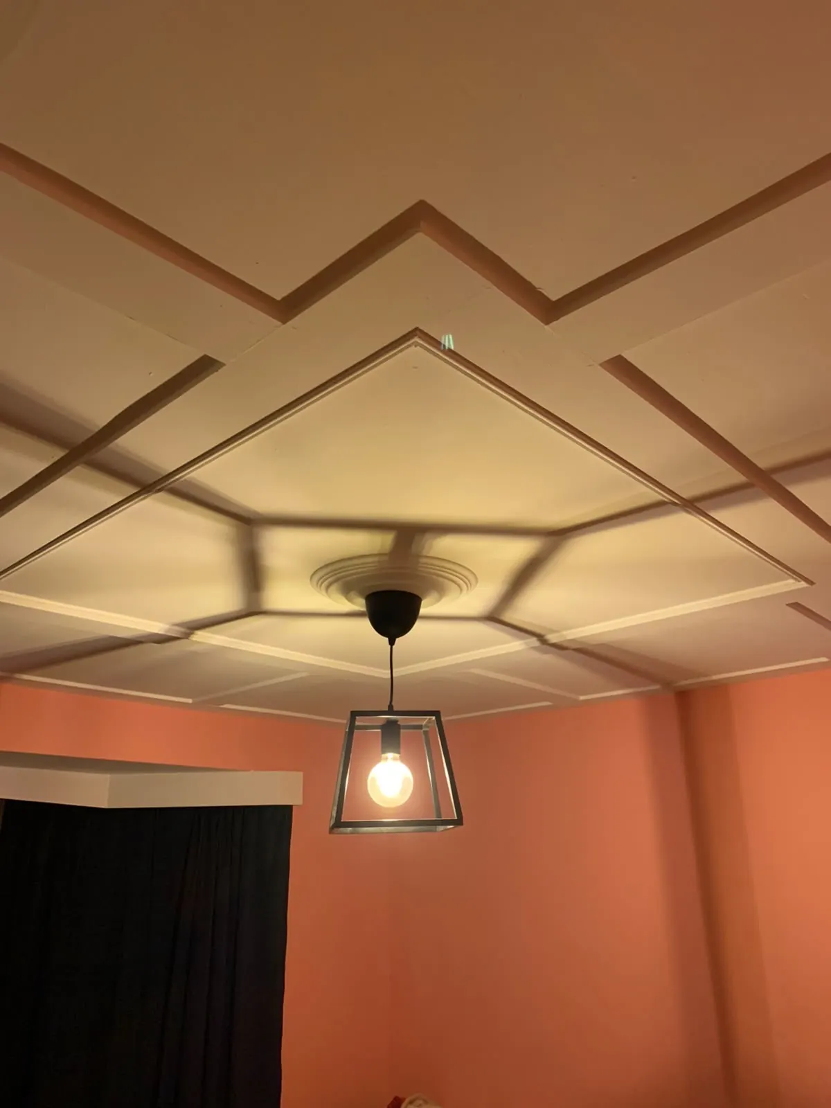 Geometric ceiling panelling around a pendant light in a dining room